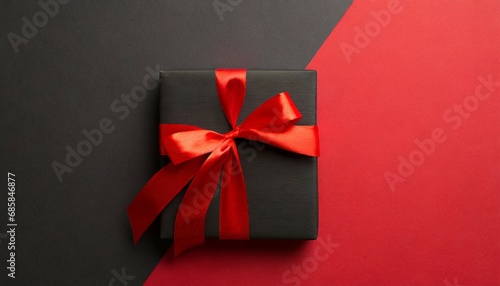 top view photo of black giftbox with vivid red ribbon bow on two color red and black background with copyspace
