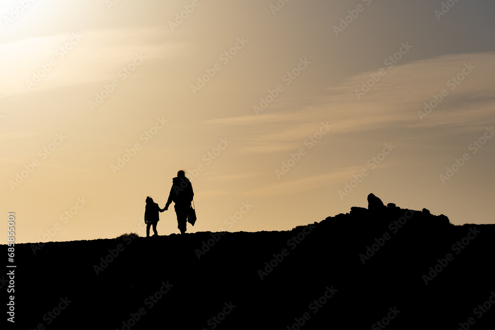 Silhouette d'une femme tenant un enfant par la main, se promenant au soleil couchant	
