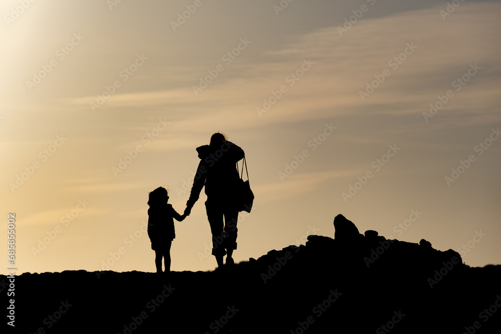 Silhouette d'une femme tenant un enfant par la main, se promenant au soleil couchant