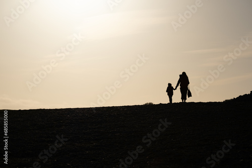 Silhouette d une femme tenant un enfant par la main  se promenant au soleil couchant  