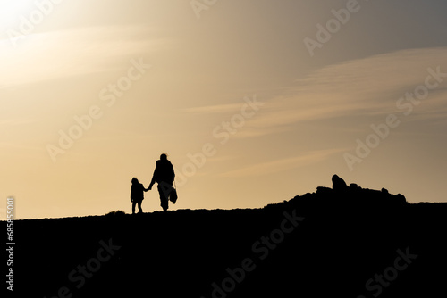 Silhouette d'une femme tenant un enfant par la main, se promenant au soleil couchant 