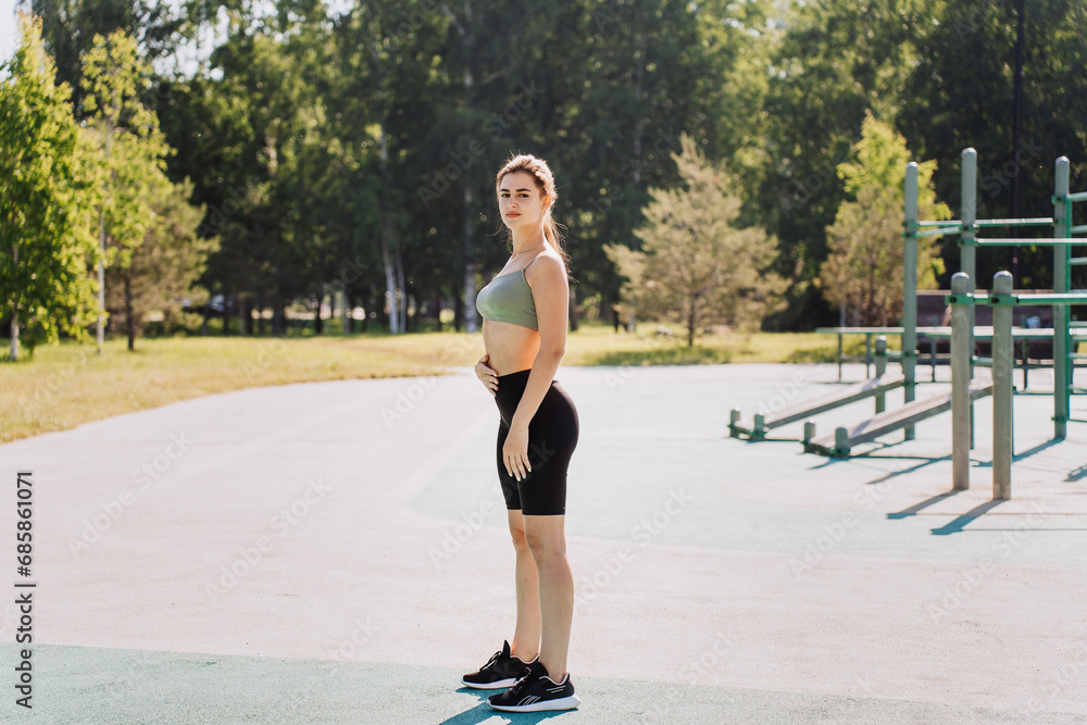 Attractive brunette fit girl in sportswear stands at sport court looks at camera. Fit hispanic young woman training outdoors at park. Fitness, workout, healthcare. Active people doing sports.
