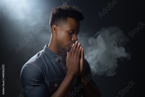 Handsome young black man praying to god with his eyes closed and clasped hands - profile side angle - God's rays of light shining down - Ethnic diversity and religion concept