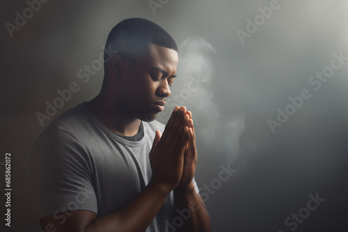 Handsome young African american man praying to god with his eyes closed and clasped hands - profile side angle - God's rays of light shining down - Ethnic diversity and religion concept