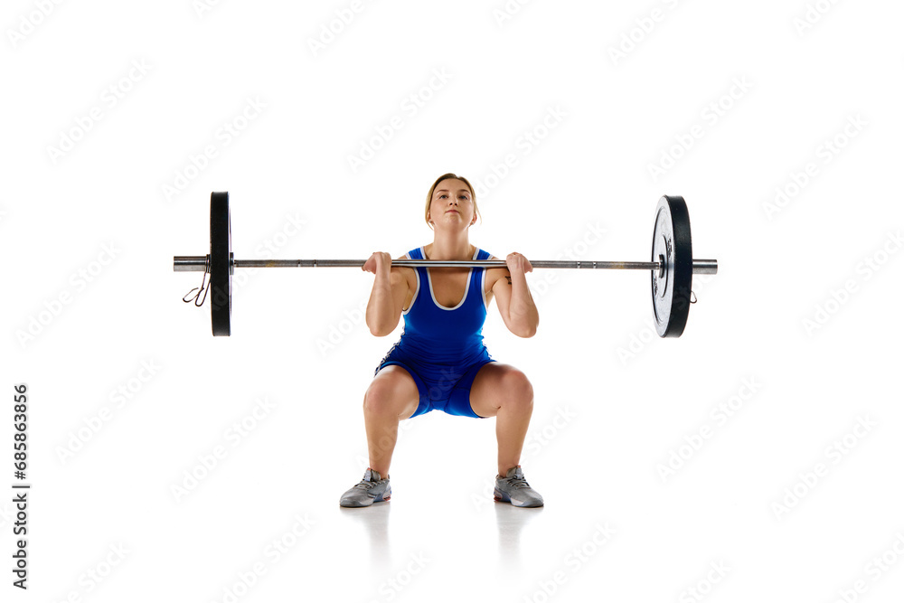 Concentrated strong young woman, athlete training doing squats, lifting heavy barbell against white background. Concept of sport, strength, gym, healthy lifestyle, power and endurance, weightlifting. Concentrated strong young woman, athlete training doing squats, lifting heavy barbell against white background. Concept of sport, strength, gym, healthy lifestyle, power and endurance, weightlifting.