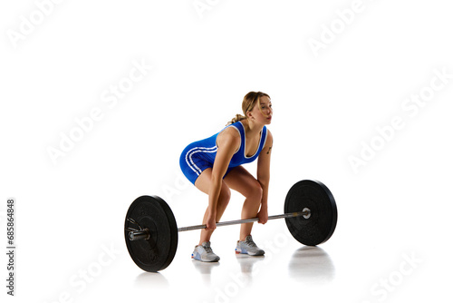 Young athletic girl, weightlifter training, lifting heavy weight, barbell against white background. Concept of sport, strength, gym, healthy lifestyle, power and endurance, weightlifting.