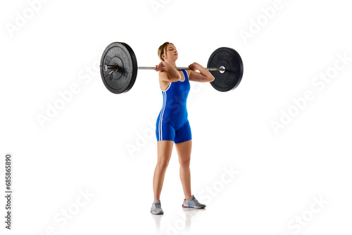Young girl with fit strong body, athlete training, lifting heavy weights, barbell against white background. Concept of sport, strength, gym, healthy lifestyle, power and endurance, weightlifting.