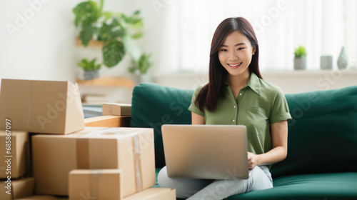 Smiling woman sitting on a green sofa with a laptop, surrounded by delivery boxes © MP Studio