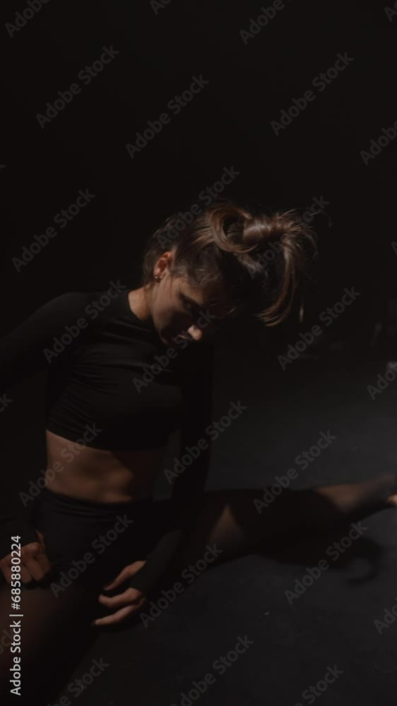 A young lady, surrounded by dim light, performs a contemporary dance routine in the studio. A young lady, surrounded by dim light, performs a contemporary dance routine in the studio.