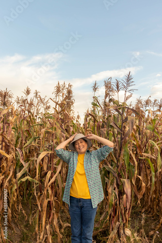 granjera con gran sonriza con la mano sujetando su sombrero de paja lista para lanzarlo por los aires esta parada frente a un sembrío de cañas de maíz seco, mujer adulta en sus 50 años feliz y empoder photo