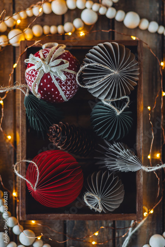 Cozy atmospheric photo, home festive atmosphere. Collection of old fashioned christmas new year foldable honeycomb toys, craft holiday decoration in vintage wooden box. Magic lights on background