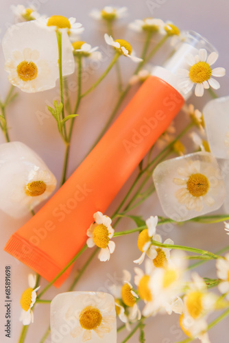 Orange cosmetic tube and chamomile flowers