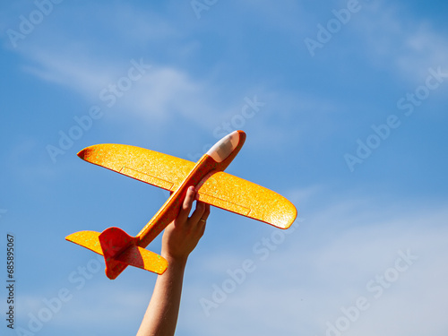 A bright toy airplane in hand against a background of blue sky on a sunny day