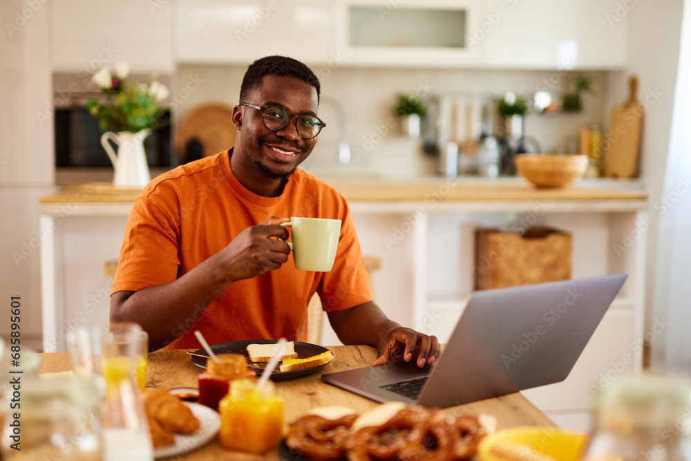 African American man using laptop while enjoying breakfast at home African American man using laptop while enjoying breakfast at home