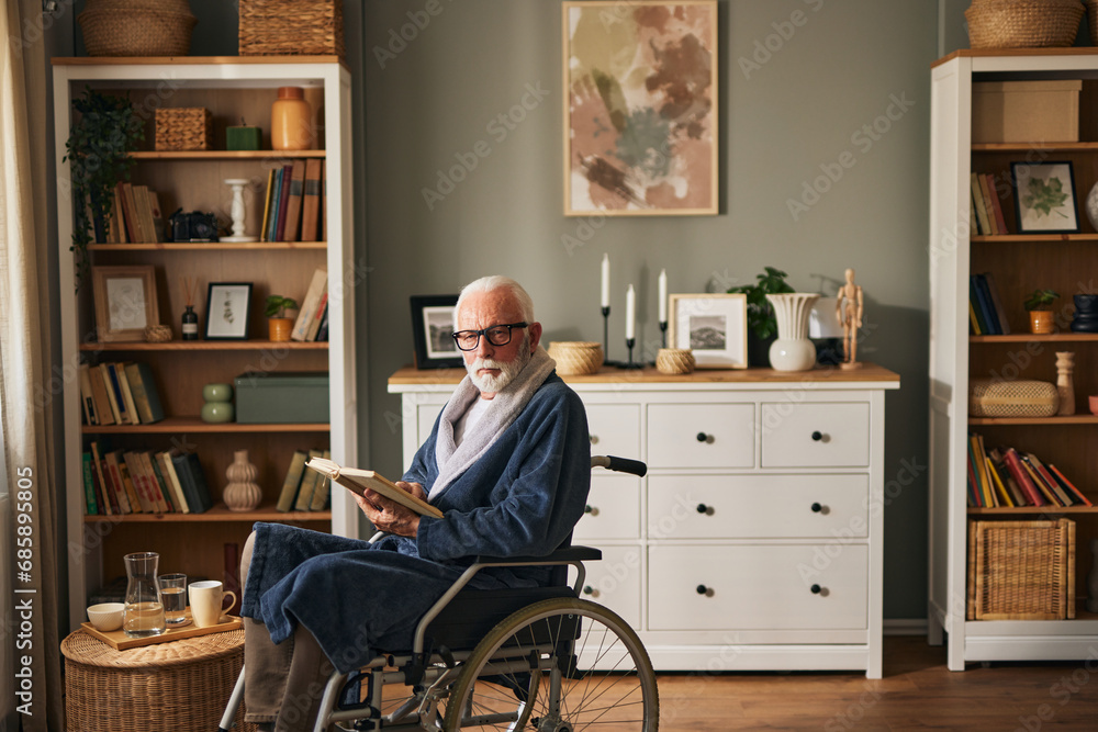 Elderly man in wheelchair reading a book at home Elderly man in wheelchair reading a book at home