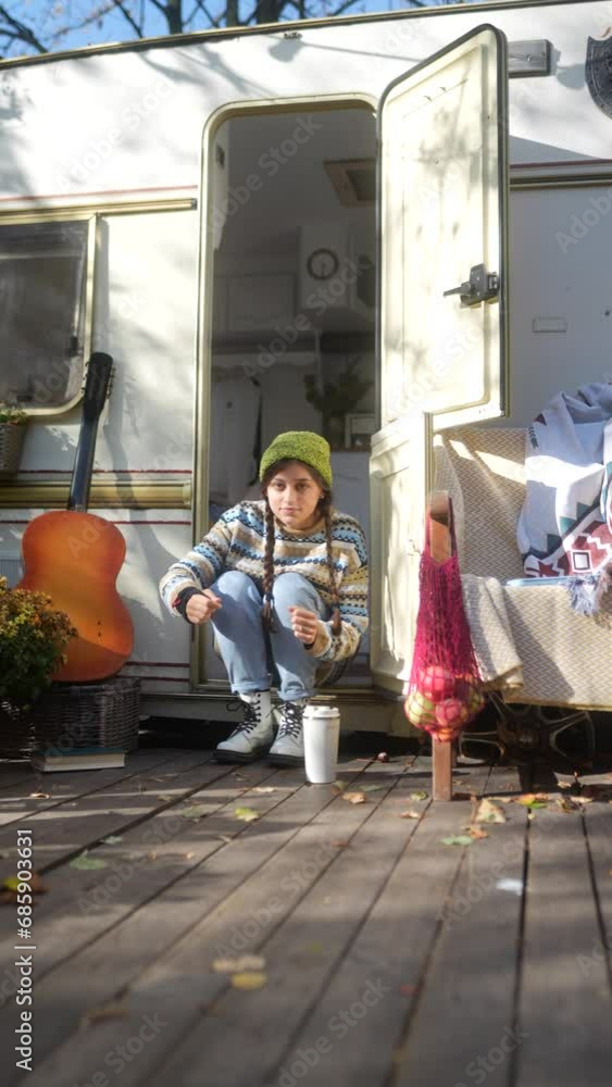 A fashionable, young hippie girl with a guitar and a thermos of hot beverage on the terrace of the trailer in the autumn garden. A fashionable, young hippie girl with a guitar and a thermos of hot beverage on the terrace of the trailer in the autumn garden.