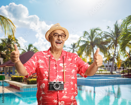 Male tourist with a camera around nech gesturing thumbs up at the pool photo