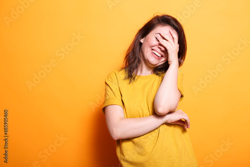 Portrait of beautiful brunette woman laughing while covering eyes and face. Enthusiastic lady using hand to hide from camera, feeling shy and happy standing over isolated background.