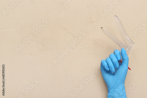 Hand in medical glove and with gynecological speculum on beige background photo