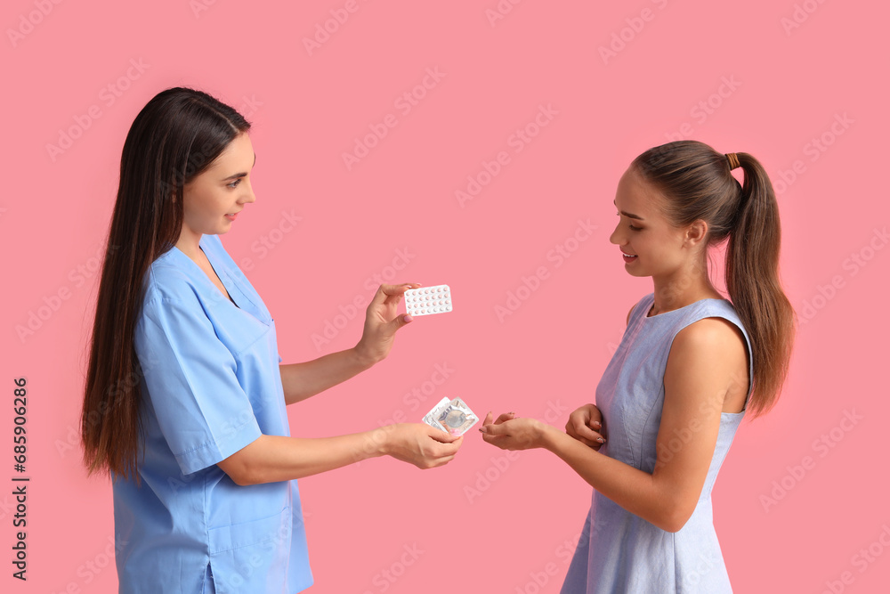 Female gynecologist giving contraceptive pills and condoms to patient on pink background Female gynecologist giving contraceptive pills and condoms to patient on pink background