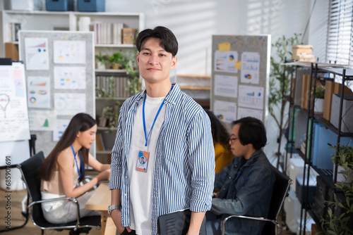 Portrait creative Asian businessman holding digital tablet laptop at at creative office workplace. team in meeting in background