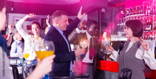 Cheerful businessman with female colleague dancing and drinking alcohol, having fun at office party in nightclub