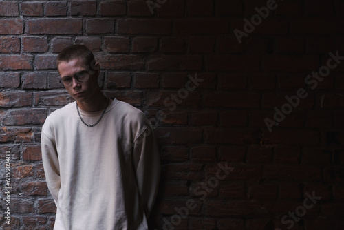 Young man in hoodie and jeans against a brick wall, light gradient.