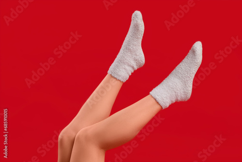 Legs of young woman in white warm socks on red background