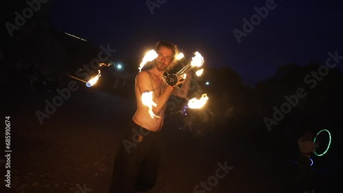 Fire show performance. Handsome male fire juggler performing with a burning contact dragon staff. Close-up. Slow motion photo