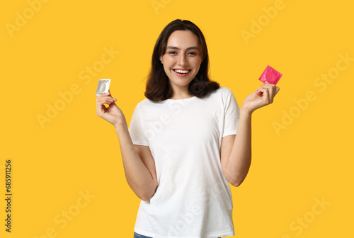Young woman with condoms on yellow background. Safe sex concept photo