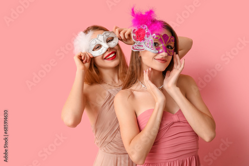 Beautiful young women in carnival masks on pink background