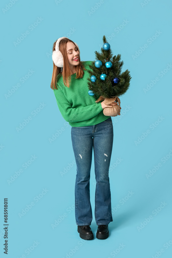 Happy young woman holding Christmas tree with balls on blue background Happy young woman holding Christmas tree with balls on blue background