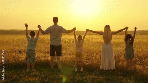 Happy family raise their hands outdoor at sunset. Teamwork of group of people  walk in park. Child mom dad walking holding hands. Group prayer sun. Family holiday. Parents child holding hands together