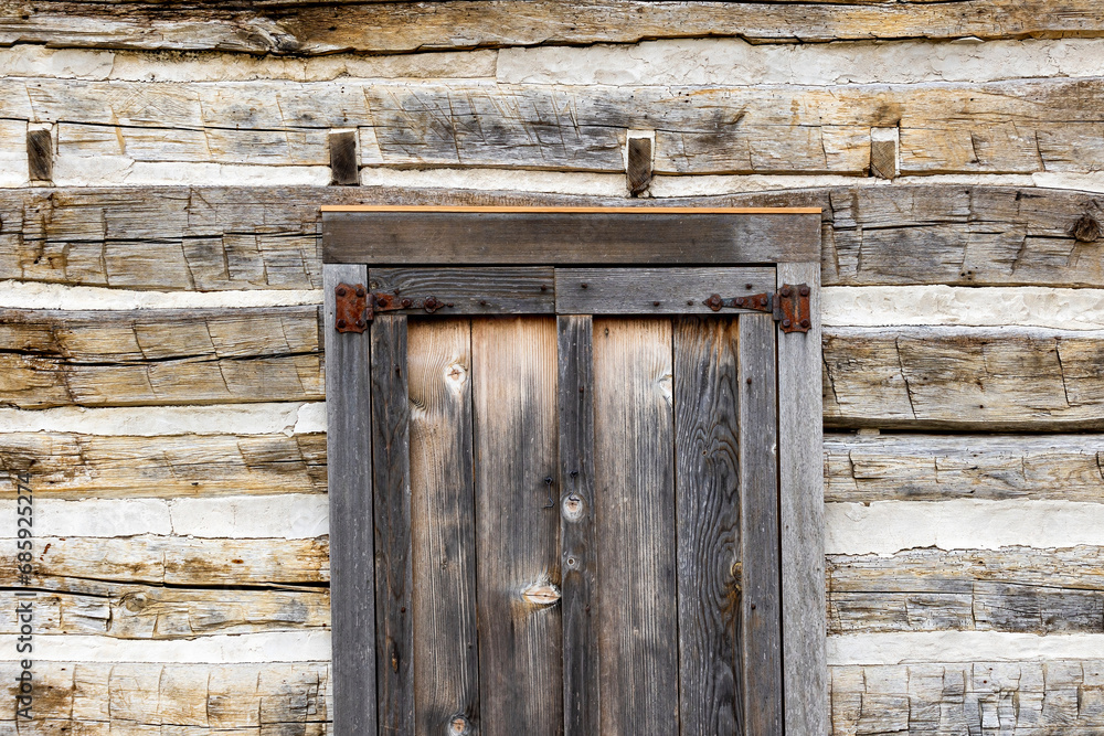 The wall of a log cabin, and an old window with hinges on the shutters. The wall of a log cabin, and an old window with hinges on the shutters.
