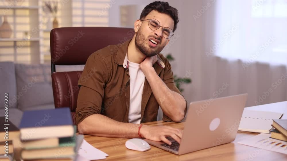 Overworked tired indian man freelancer or student with severe neck shoulder pain after hard work on laptop computer at home workplace Sad male with glasses suffers from tension in the spine indoors Overworked tired indian man freelancer or student with severe neck shoulder pain after hard work on laptop computer at home workplace Sad male with glasses suffers from tension in the spine indoors