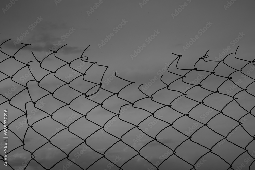 Looking up at a chain link fence with blue sky and clouds. wire fence. Chain link fence see sky. Opening in metallic fence. blue sky. Challenge. breakthrough concept. Looking up at a chain link fence with blue sky and clouds. wire fence. Chain link fence see sky. Opening in metallic fence. blue sky. Challenge. breakthrough concept.