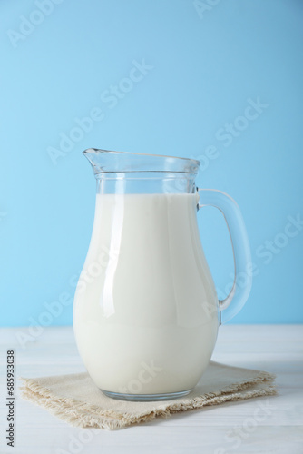 Jug of fresh milk on white wooden table against light blue background
