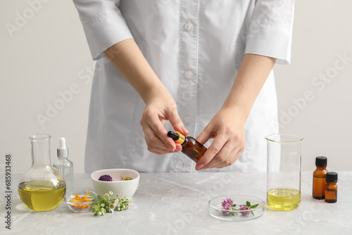 Scientist developing cosmetic oil at light grey table, closeup