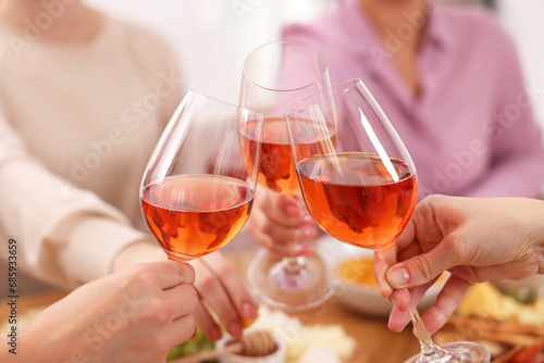 People clinking glasses with rose wine above table indoors, closeup