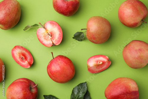 Tasty apples with red pulp and leaves on light green background, flat lay