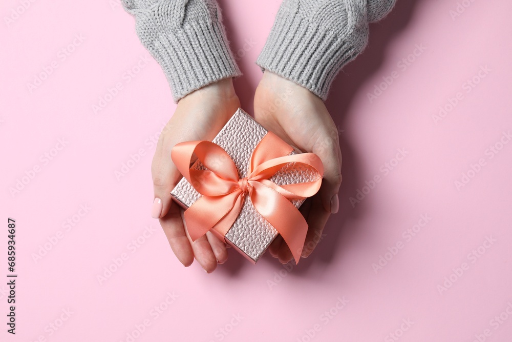 Christmas present. Woman holding gift box on pink background, top view