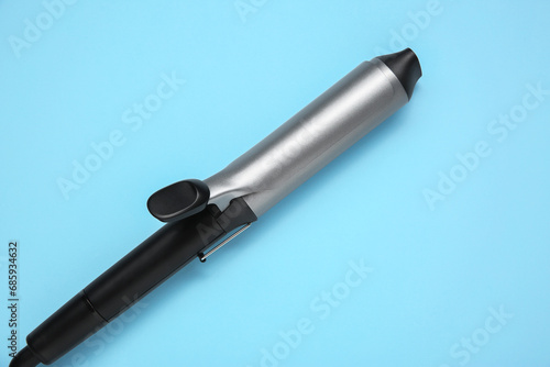 Hair styling appliance. One curling iron on light blue background  top view