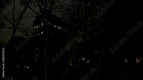 Nightime Apt building with lit windows seen through trees - urban - establishing shot