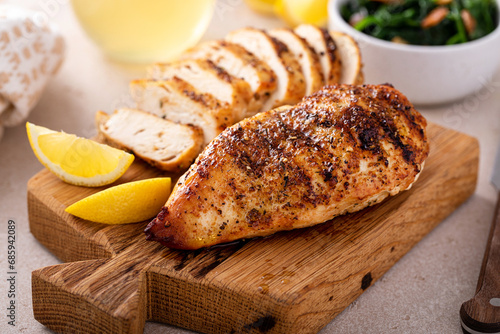 Grilled chicken breast whole and sliced on a cutting board with lemon