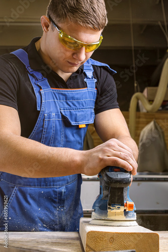 Portrait of a  young man  carpenter using electric sanding machine to polish a wood barin workshop photo