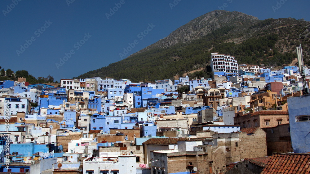 Blue and white buildings on a hill in the medina, with a mountain peak in the background, in Chefchaouen, Morocco