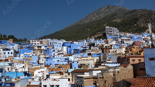 Blue and white buildings on a hill in the medina, with a mountain peak in the background, in Chefchaouen, Morocco © Angela