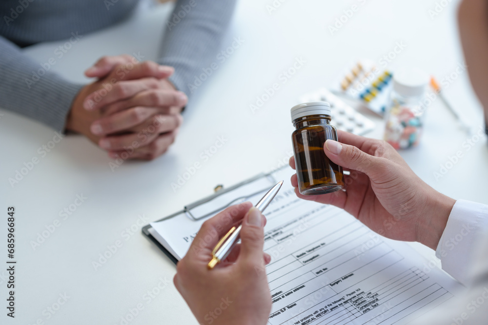 Doctor, pharmacist pointing at pill bottle, giving advice, recommending how to take medicine to female patient, explaining prescription to business woman Medical and health care system. - obrazy, fototapety, plakaty 