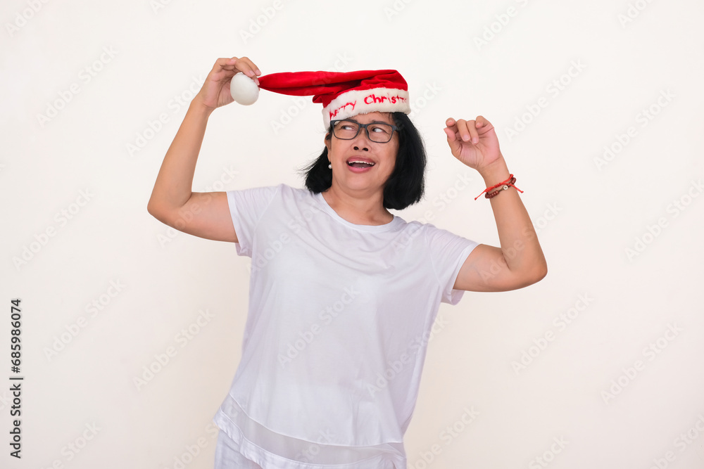 An Asian woman in white is wearing Santa Klaus's hat; glancing up, smiling. An Asian woman in white is wearing Santa Klaus's hat; glancing up, smiling.