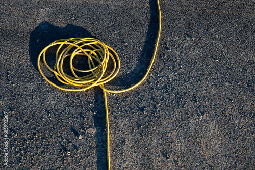 Heavy gage yellow electrical extension cord running over an asphalt street

